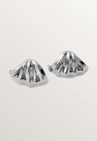 Piezas decorativas de metal plateado con forma de conchas onduladas, que presentan una textura acanalada y bordes curvados, reflejando la luz.