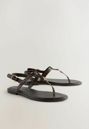 Sandales en cuir brun avec un design de bride tongs, dotées de brides de cheville croisées et d'accents en métal doré. Semelle plate.