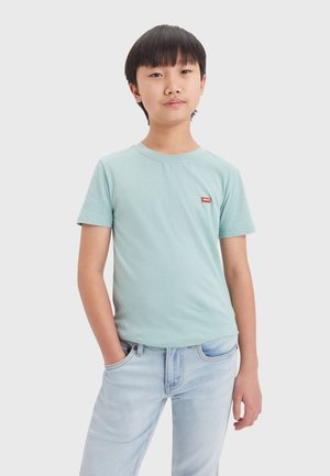 Camiseta de algodón de color azul claro con mangas cortas, escote redondo y un pequeño parche con el logo rojo de Levi's en el lado izquierdo del pecho. Combinada con jeans de mezclilla claros.