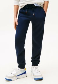 Marineblå sweatpants med elastisk talje og snøre. Har sidelommer og tapered cuffs. Kombineret med hvide sneakers med blå accenter.