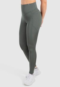 Wysokie legginsy sportowe w ciemnozielonym kolorze, z gładką fakturą, dopasowanym krojem i kontrastowymi szwami.
