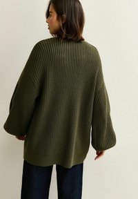 Oversized sweter w oliwkowym kolorze z fakturowanym wzorem dzianiny, opadającymi ramionami i szerokimi rękawami. Ribbowane wykończenie dołu i mankietów dodaje szczegółu.