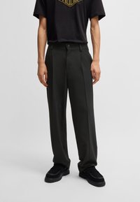 Dark green tailored trousers with a straight cut, featuring a button closure and side pockets, paired with a black graphic t-shirt.