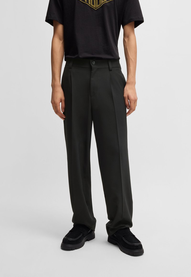 Pantaloni încărcați de tip tailored, de culoare verde închis, cu croială dreaptă, având închidere cu button și buzunare laterale, asortați cu un tricou negru cu grafică.