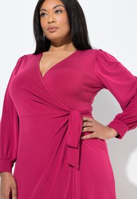 Abito avvolgente fucsia con maniche lunghe a sbuffo, scollatura a V e un nastro in vita, realizzato in tessuto morbido ed elastico.