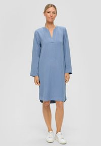 Lichtblauwe lange mouw jurk met een notch halslijn, gemaakt van zachte stof, met een losse fit en rechte zoom, gedragen met witte sneakers.