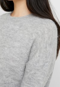 Hellgrauer, weicher Strickpullover mit rundem Ausschnitt und dezenter Struktur. Sichtbare Schulternaht mit locker geschnittenem Design.