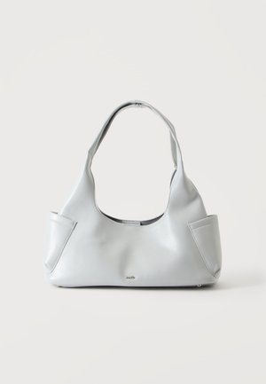 Sac à main en cuir gris clair avec une seule poignée incurvée et de petites poches extérieures de chaque côté sur un fond uni.