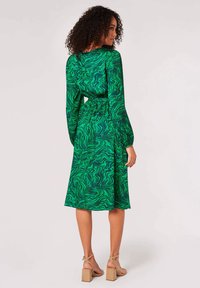 Robe midi verte avec un motif ondulé, manches longues et taille cintrée. Le matériau semble léger avec une texture lisse.