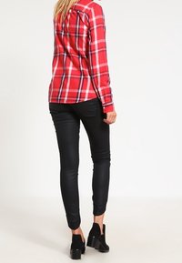 Röd och svart rutmönstrad långärmad skjorta, matchad med svarta stretchbyxor och svarta ankelstövlar, sedd bakifrån.