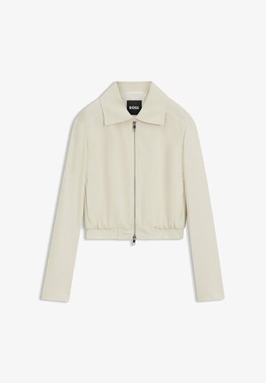 Veste beige clair zippée avec col pointu, manches longues et taille élastique, estampillée avec l’étiquette "BOSS" à l’intérieur du col.