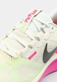 Baskets de course Nike avec une tige en mesh légère couleur crème, des accents colorés en vert et rose, un swoosh noir et une semelle rembourrée rose.