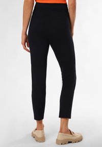 Marineblaue, taillierte Hose mit hoher Taille, gerippter Textur und zwei Gesäßtaschen. Kombiniert mit beigen Schuhen mit dickem Profil.