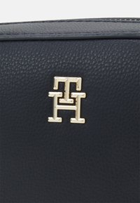 Borsa in pelle blu navy con superficie texturizzata e dettaglio del logo geometrico dorato. Rifinita con cuciture lungo i bordi.