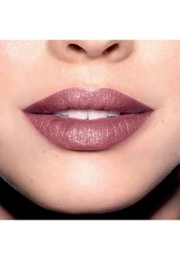 Rouge à lèvres mauve mat sur des lèvres pleines, mettant en valeur une texture lisse avec un éclat subtil. La peau est claire et l'arrière-plan est sombre pour le contraste.