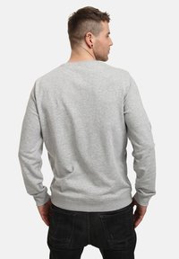 Šedá mikina z měkké látky, s dlouhými rukávy, kulatým výstřihem a žebrovaným lemem. Bez viditelných grafických prvků nebo vzorů.