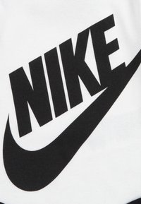 Baltas audinys su dideliu juodu "NIKE" užrašu ir swoosh logotipu. dizainas yra ryškus su aiškia kontrastu ir sklandžia tekstūra.
