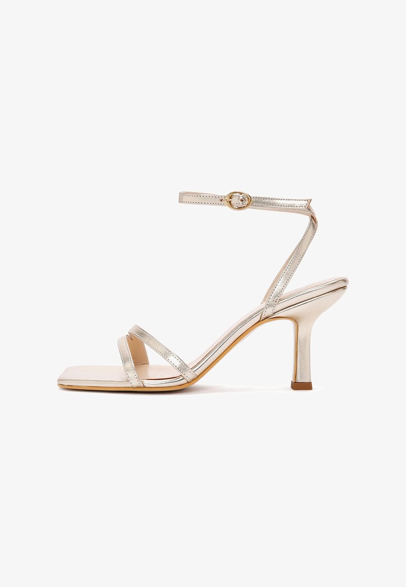 Sandalia metálica dorada de tacón alto con tiras delgadas, hebilla en el tobillo, punta cuadrada y tacón delgado de altura media.