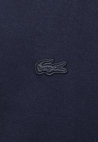 Navy blue cotton fabric with a ribbed texture featuring an embroidered dark logo in the shape of a crocodile. Simple and streamlined design.