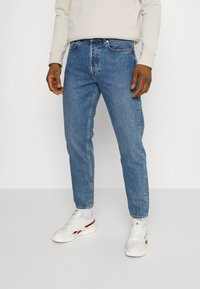 Jasnoniebieskie dżinsy o prostym kroju, z pięcioma kieszeniami i subtelnymi przetarciami. Połączone z białymi sneakerami.