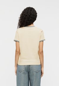 Κρεμ κοντομάνικη μπλούζα με γκρι περιμετρική λεπτομέρεια στον γιακά και τα μανίκια, κατασκευασμένη από απαλό ύφασμα· συνδυασμένη με ανοιχτό μπλε τζιν παντελόνι με φαρδιές παντελόνες.