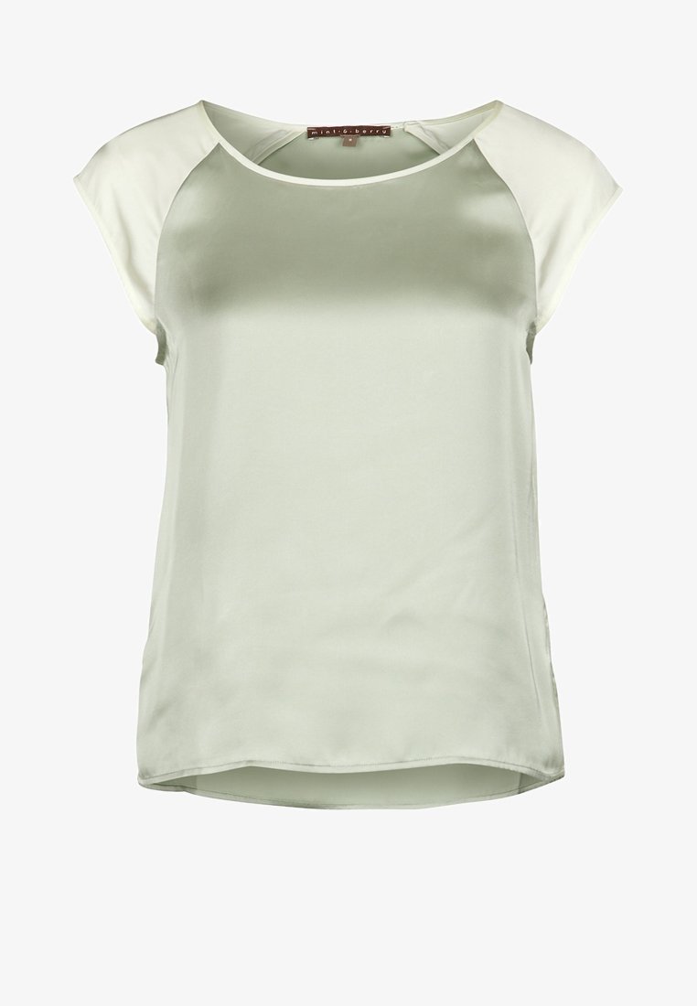 Blouse verte en satin avec manches raglan courtes crème, encolure ronde et ourlet légèrement courbé. Texture lisse et design décontracté.