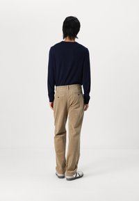 Marineblaues Langarmshirt mit Rundhalsausschnitt, kombiniert mit beigen Cordhosen mit Gesäßtaschen und einem leicht lockeren Schnitt. Weiße und schwarze Sneakers.