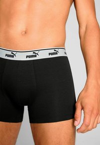 Black cotton boxer shorts featuring a light gray waistband with black Puma branding. The fabric has a smooth texture and a fitted design.