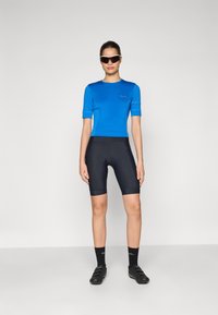 Blå kortärmad cykeltröja i kombination med svarta vadderade shorts, med en åtsittande design och andningsbart material, accentuerat av svarta skor.