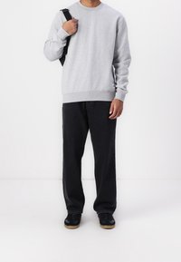 Sweat-shirt en coton gris avec poignets et ourlet côtelés, associé à un pantalon en denim noir ample et des baskets noires à semelles marron.