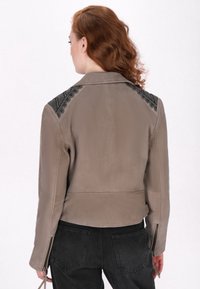 Jachetă din piele taupe cu accente negre cu model pe umeri, design scurt, manșete cu fermoar și textură netedă.