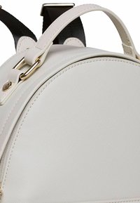 Weißer Rucksack mit runder Form, gefertigt aus strukturiertem Material und mit glatter Oberfläche, goldfarbigen Akzenten und zwei Tragriemen.