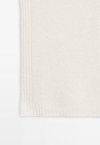 Gehaakte crèmekleurige sjaal met een zachte textuur, voorzien van ribbel uiteinden en strakke lijnen, wat eenvoud en warmte benadrukt.