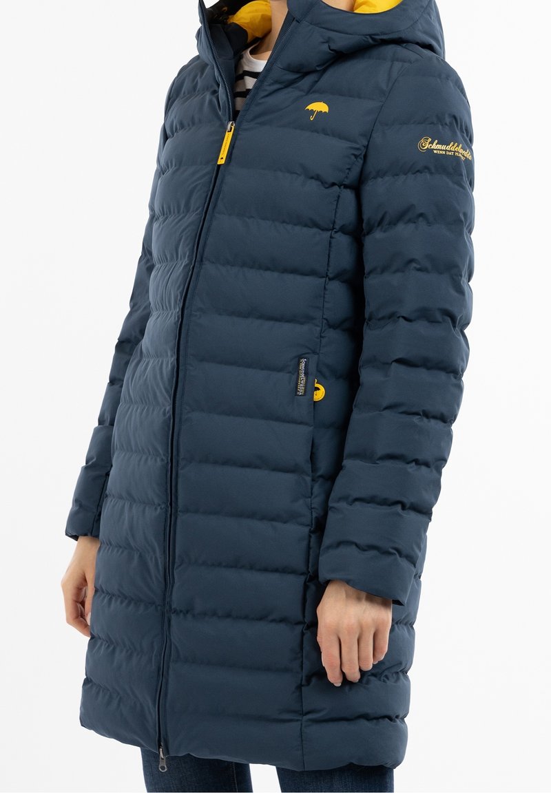 Námořnický pufový kabát se zapínáním na zip, žlutou podšívkou kapuce a logem. Obsahuje prošívaný design a boční kapsy pro zahřátí.