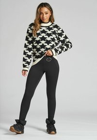 Maglione a motivo stellato in bianco e nero, abbinato a leggings neri con logo. L'outfit è completato da stivali alla caviglia imbottiti neri.