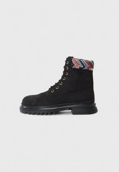 Botín de ante negro con un puño de textura multicolor, ojales metálicos y una suela de goma resistente. Presenta un diseño de cordones.