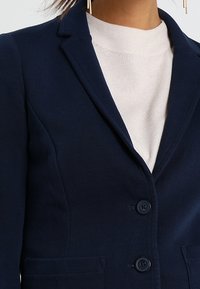 Marinblå blazer med kavajkrage, två knappar och framfickor. Slät tyg med en strukturerad design. Lättviktig med en minimalistisk look.