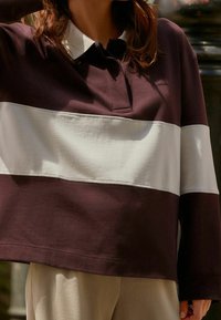 Langarm-Polohemd mit burgunderfarbenem Oberkörper und einem weißen horizontalen Streifen. Hergestellt aus weichem Baumwollstoff, mit klassischem Kragen und Knopfdetails.
