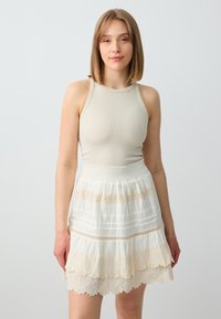 Débardeur crème à côtes associé à une jupe blanche à plusieurs couches avec des bordures en dentelle et des bandes décoratives. Le tissu a une apparence douce et texturée.