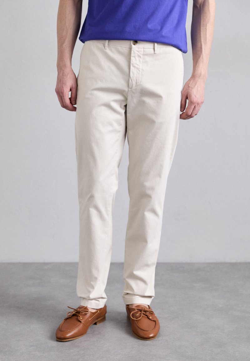 Beige cotton trousers with a straight fit, featuring a single button closure and two front pockets, paired with brown leather shoes.