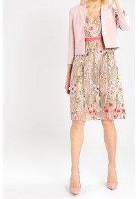 Rosa jacka över en blommigt broderad klänning med figursydd överdel och utsvängd kjol. Klänningen har färgglada mönster och en markerad midja.