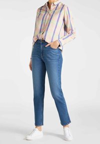 Camisa de manga larga a rayas multicolores con cuello, combinada con unos jeans ajustados azules y zapatillas blancas. Tejido texturizado, corte casual.