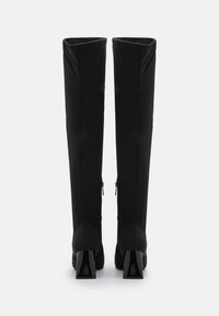 Botas negras hasta la rodilla hechas de un tejido suave, con un tacón grueso y cremalleras laterales para mayor funcionalidad. Diseño limpio y minimalista.