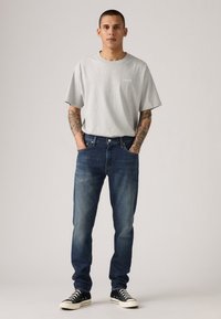 Gray short-sleeved T-shirt with a small logo, paired with dark blue denim jeans and black canvas sneakers with white accents.