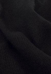 Tissu tricoté noir avec une texture douce, présentant un motif en relief subtil et une apparence drapée et agréable.
