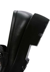 Chaussure plateforme noire avec une tige en cuir texturé, finition mate contrastante et semelle épaisse à nervures pour une adhérence et une stabilité accrues.