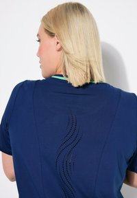 Camisa atlética de color navy con cuello y espalda verdes, decorada con un patrón ondulado de pequeños recortes para ventilación. Manga corta, textura suave.
