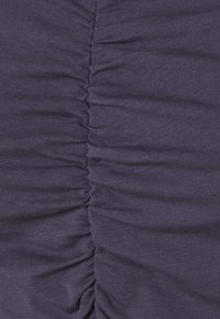 Lila tyg med horisontella rynkdetaljer, som har en mjuk, texturerad yta. Tyget är stickat och sträcker sig något.