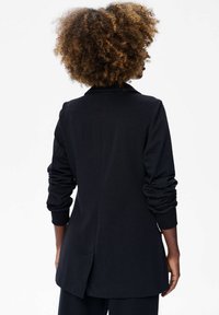 Zwarte blazer gemaakt van zachte stof, met een relaxte pasvorm, lange mouwen met gathers aan de manchetten en een rugventilatie voor extra bewegingsvrijheid.