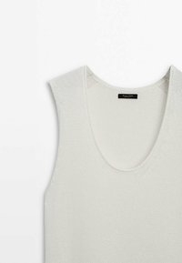 Haut sans manches en tricot beige clair avec un col dégagé. Le tissu texturé présente une maille lâche et un motif diagonal subtil.